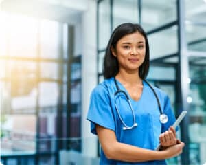 Young nurse wearing stethoscope and carrying tablet in hospital setting
