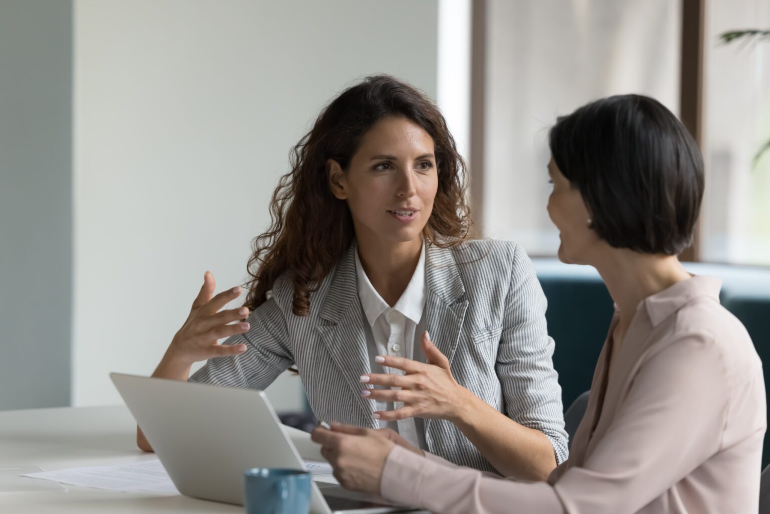 Two businesswomen sitting at a desk with a laptop in discussion