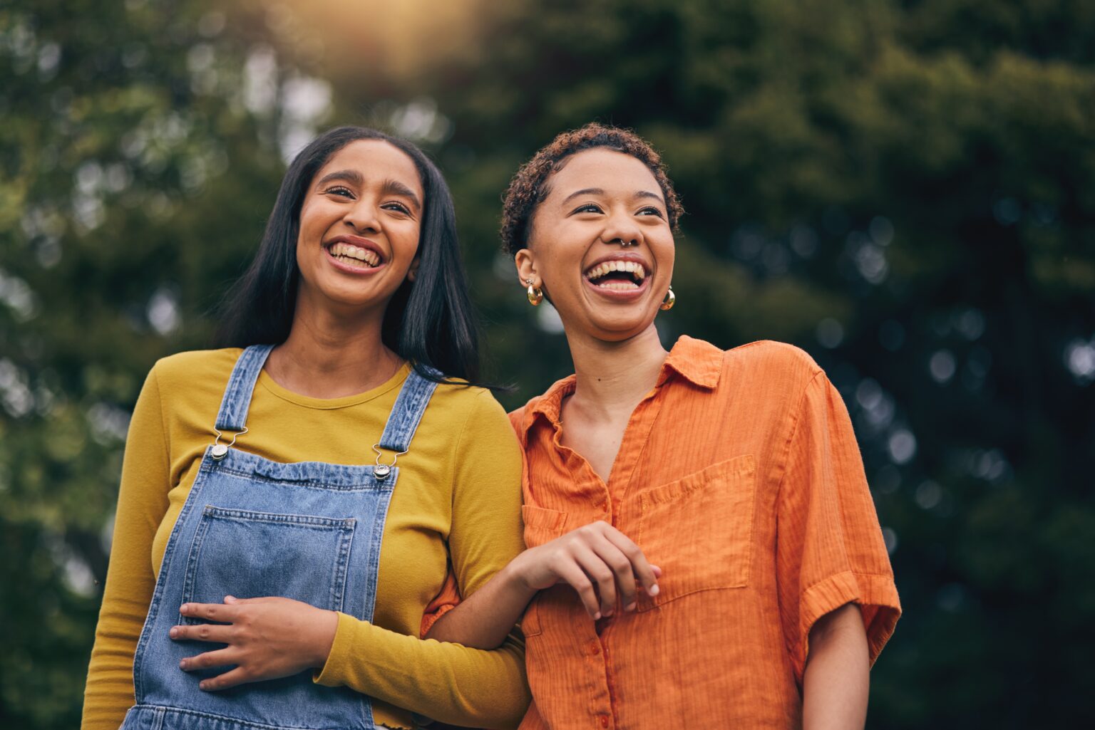 Two young friends walking in the park arm-in-arm laughing