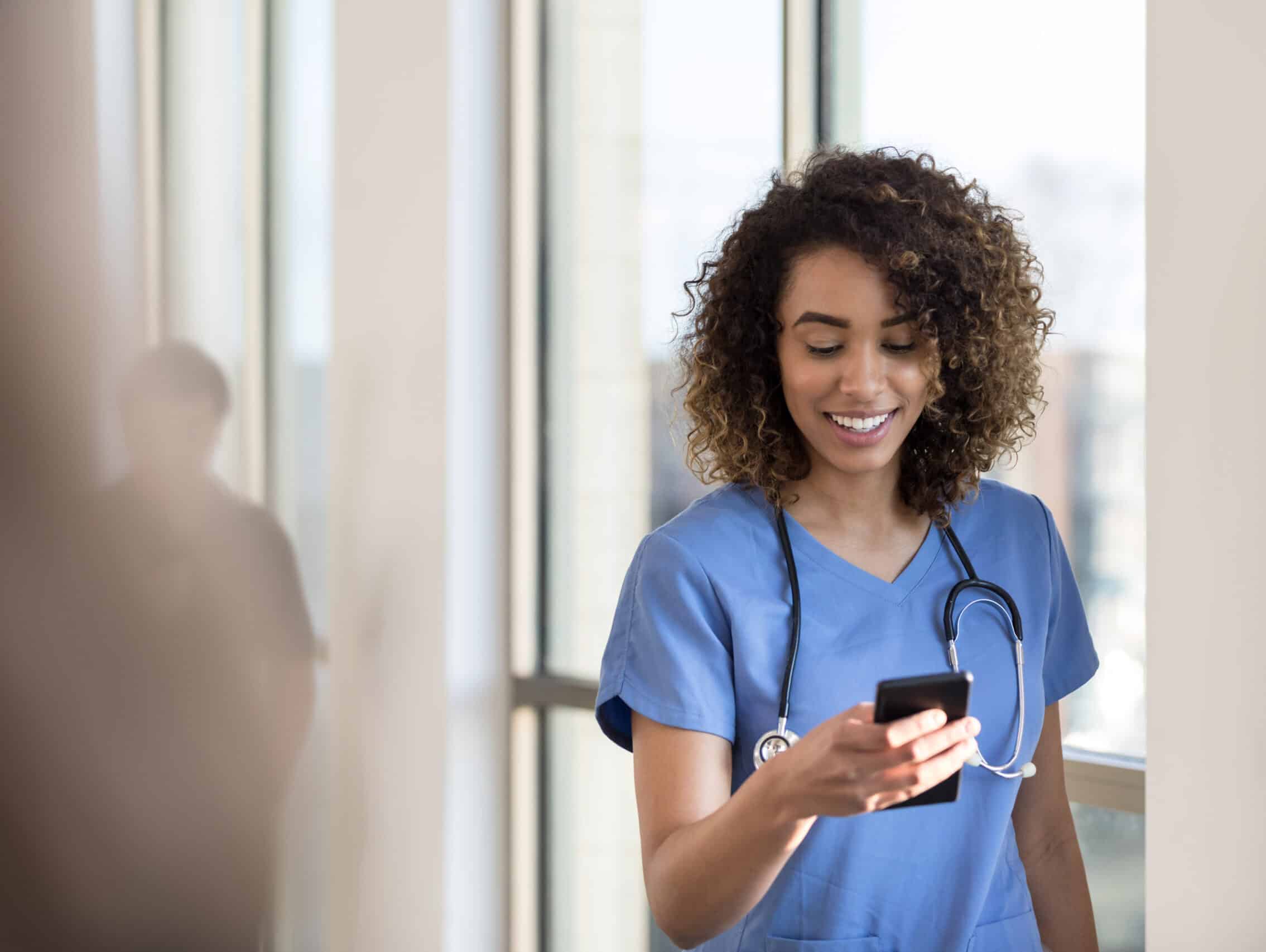 Attractive young female nurse checks smartphone as she walks in a hospital hallway