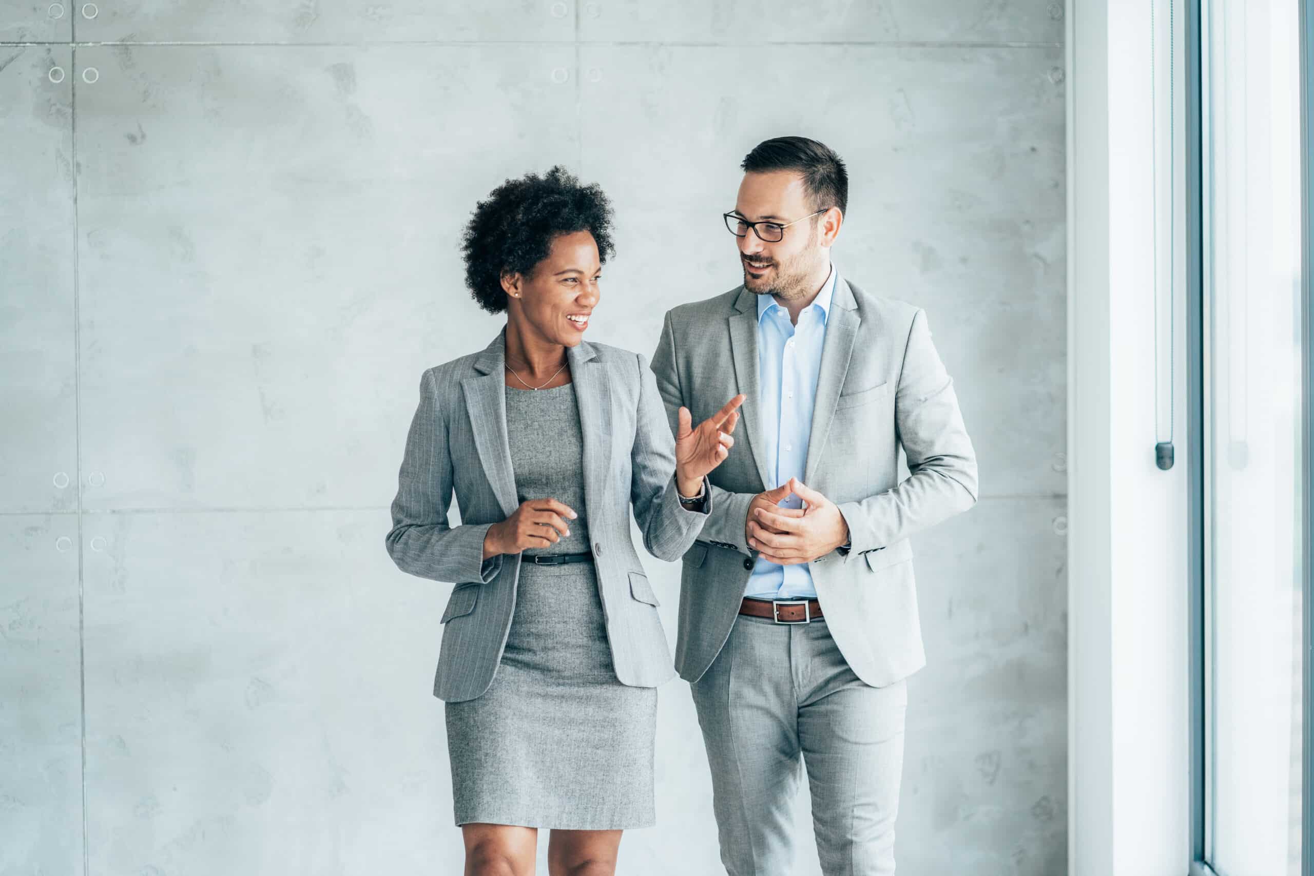 Two smiling business people walking through office hall and talking