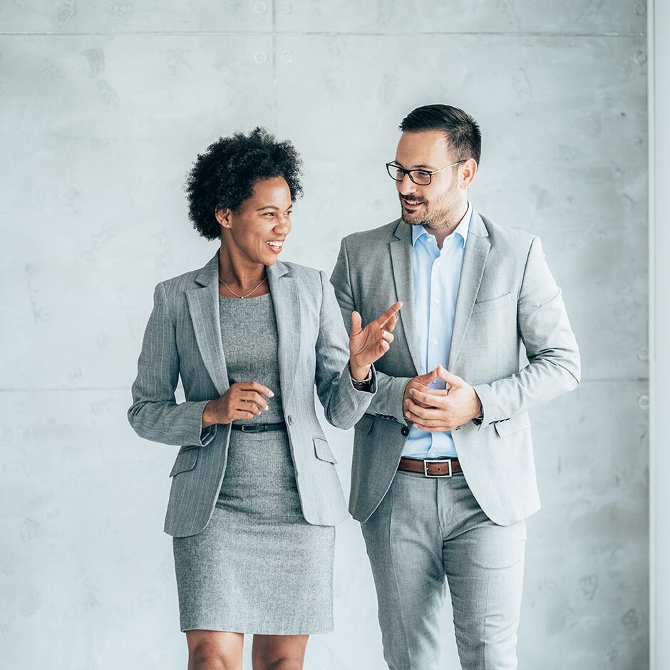 Two smiling business people walking through office hall and talking