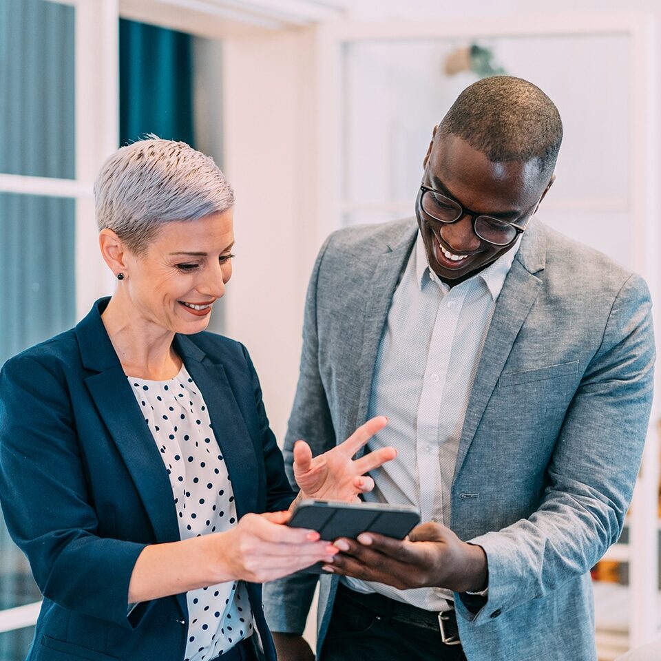 Shot of two successful businesspeople working together on a tablet in modern office. Businessman and businesswoman in meeting using digital tablet and discussing business strategy. Two business people talking in the office.