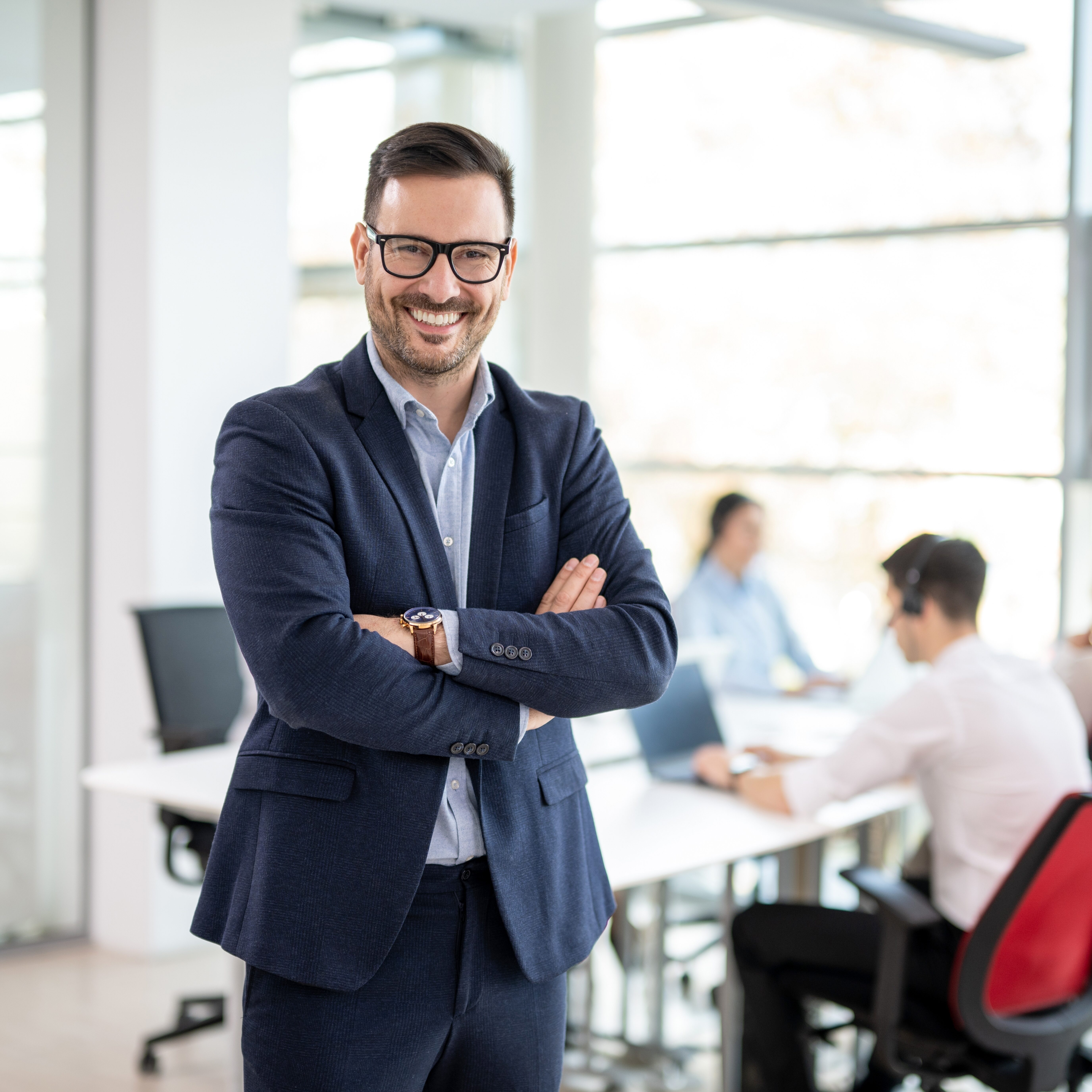 Confident businessman standing with crossed arms in front of a meeting room full of people