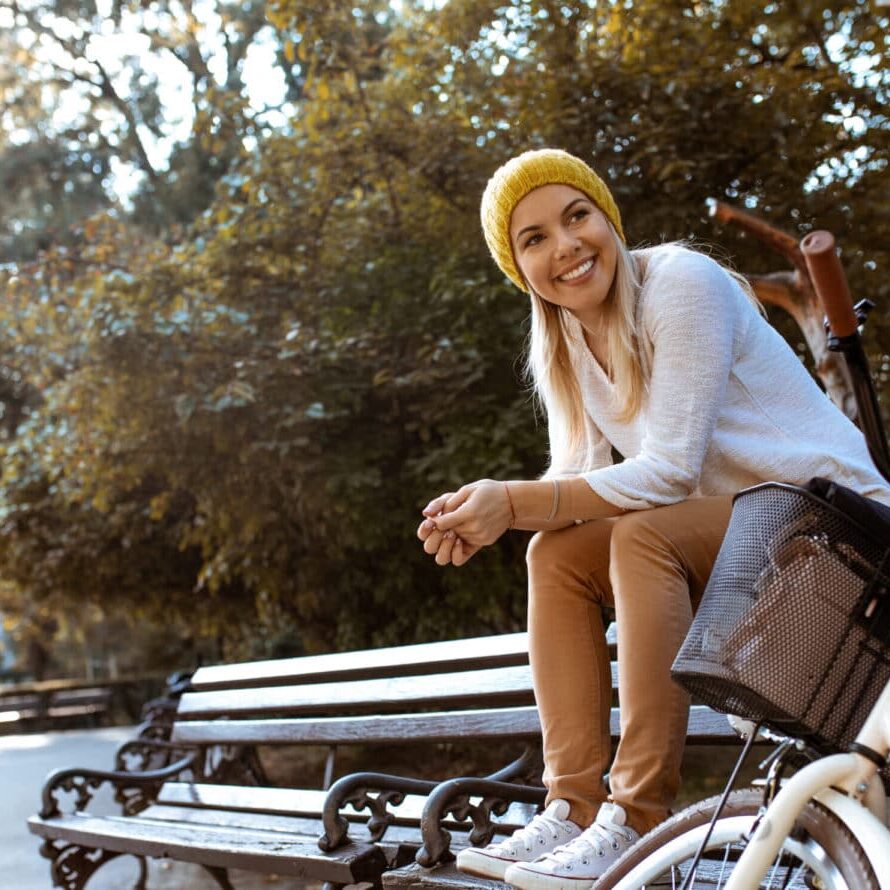 Young woman sitting on park bench next to parked bicycle