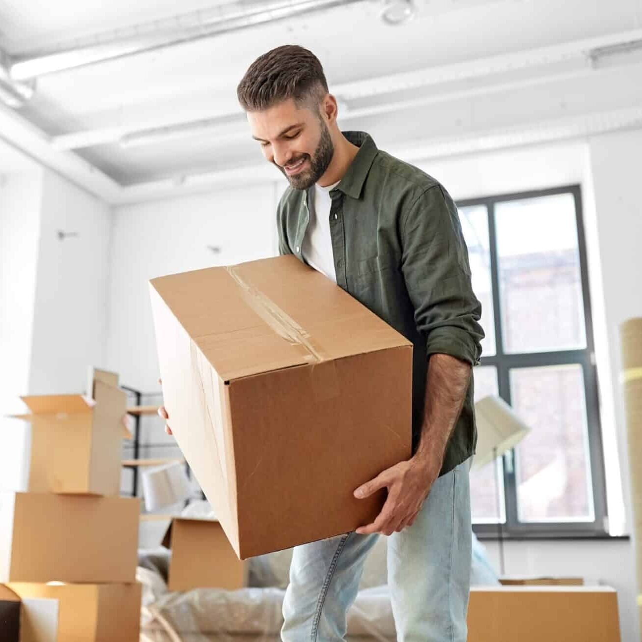 Happy smiling young man carrying moving box into new home